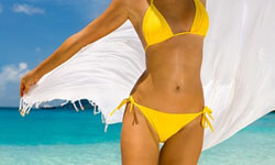 Picture of a woman, happy with her abdomen and waist  liposuction procedure she had with Top Plastic Surgeons in beautiful San José, Costa Rica.  The woman is wearing a two piece yellow bathing suit and walking through the surf at the beach.