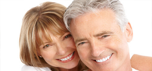 Close-up picture of a smiling couple looking directly into the camera showing their happiness with  the plastic surgery they had done in Costa Rica.  The woman has medium brown hair and the man has white hair.
