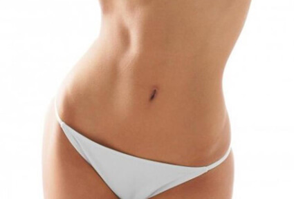 Picture of a woman facing the camera and happy with the perfect abdomen liposuction procedure she had with top plastic surgeons in beautiful San José, Costa Rica.  She is wearing a two piece bikini and showing a flat abdomen to the camera.