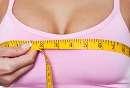 Picture of a woman measuring her breasts with a tape measure, and happy with the perfect breast reduction procedure she had with  top plastic surgeons in beautiful San José, Costa Rica.  She is wearing a light purple top and facing the camera.