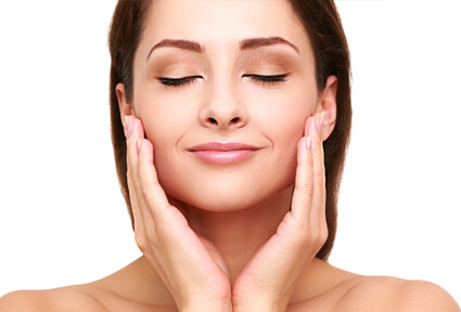 Picture of a woman with long dark brown hair, facing the camera with eyes closed, holding her hands to the side of the cheeks and happy with her perfect face lift with neck lift procedure she had with top plastic surgeons in beautiful San José, Costa Rica.