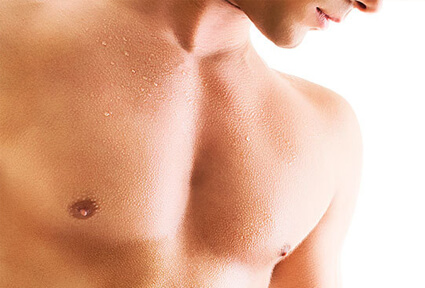 Picture of a man looking slightly away from the camera showing his chest and happy with his perfect male breast reduction procedure he had with top plastic surgeons in beautiful San José, Costa Rica.  The man is shirtless and is looking downwards.