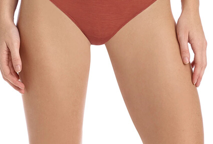 Picture of a trim woman wearing a red bikini bottom, and happy with her perfect thigh lift she had with top plastic surgeons in beautiful San José, Costa Rica.  The woman is facing the camera with both arms down to her sides.