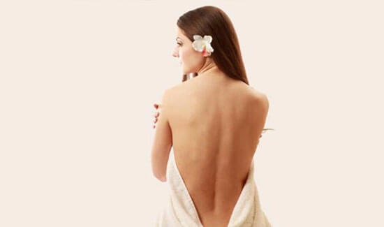 Picture of a woman sitting with her back to the camera and happy with her perfect back liposuction procedure she had with Costa Rica MedVentures in beautiful San José, Costa Rica.  The woman has a white towel draped around her.