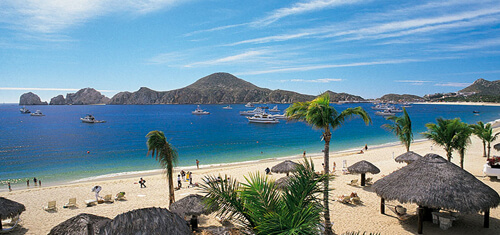 Picture of a beautiful sandy beach in Costa Rica. The picture shows small boats near the shore line and grass huts on the beach.