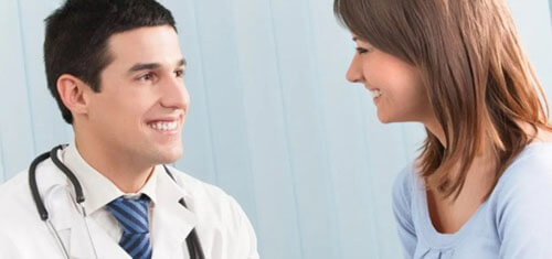 Picture of a smiling patient consulting with a smiling plastic surgeon in Costa Rica.  The patient is wearing a light blue shirt and the doctor is wearing a white smock