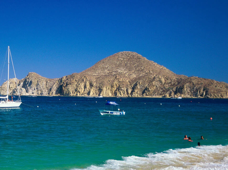 Picture of a beautiful sandy beach in Flamingo, Costa Rica.  The picture shows white sand, blue water and framed by tall rocks behind the shoreline.