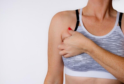 Picture of a woman facing the camera and happy with the perfect bra line liposuction procedure she had with top plastic surgeons in beautiful San José, Costa Rica.  The woman is wearing a soft light purple pastel top and holding one hand to the area of her bra line liposuction.