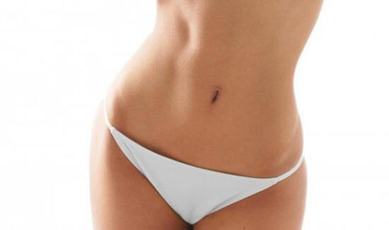 Picture of a woman facing the camera and happy with the perfect abdomen and waist liposuction procedure she had with Costa Rica MedVentures in beautiful San José, Costa Rica.  She is wearing a two piece bikini and showing a flat abdomen to the camera.