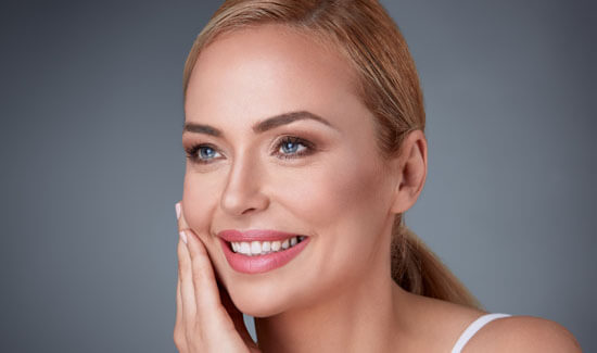 Picture of a woman, facing the camera and happy with her perfect face lift with neck lift procedure she with Costa Rica MedVentures in beautiful San José, Costa Rica.   The woman has her hand to the side of her face indicating her happiness with the face lift with neck lift.