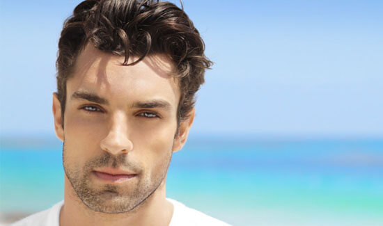 Picture of a man, facing the camera and happy with his perfect hair transplant procedure he had with Cabo MedVentures in beautiful San José, Costa Rica.  The man has a white t-shirt on and has a blue ocean as a backdrop.